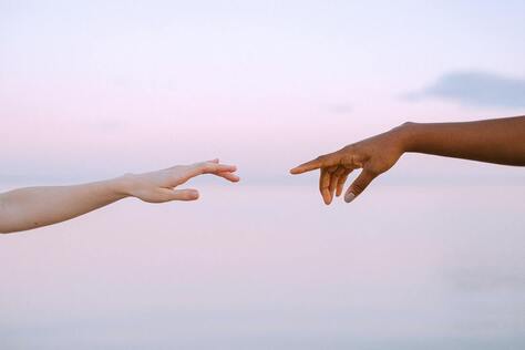 Image of two hands reaching toward each other -- one white and the other brown